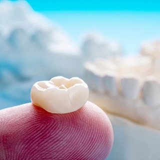 a dental technician in Orange holding a dental crown 