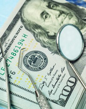 dental tools sitting on top of a stack of $100 bills on blue background
