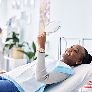 Woman smiling at reflection in handheld mirror.